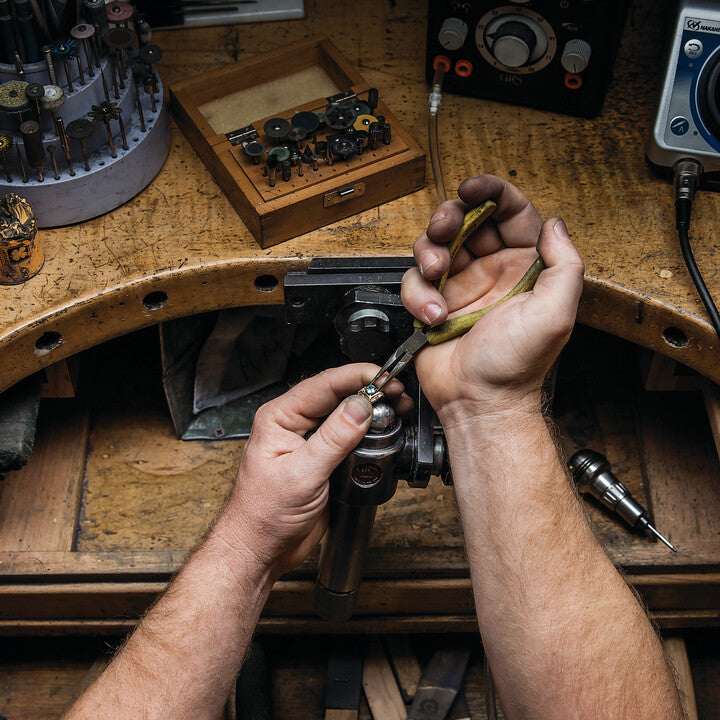 Jeweler using pliers to work on a ring at a jewelry repair bench.