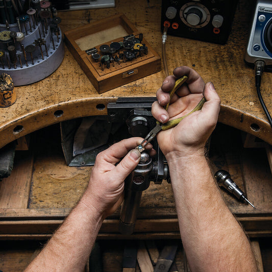 Jeweler using pliers to work on a ring at a jewelry repair bench.